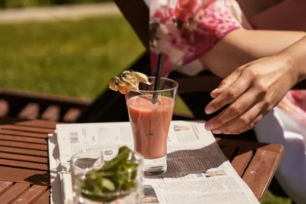 Een persoon zit aan een tafel met een drankje op een krant.