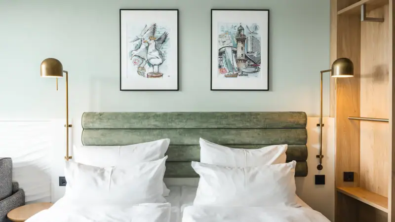 Een bed met witte kussens en een groen hoofdeinde, geflankeerd door twee lampen.