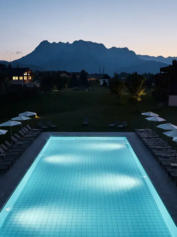 Zwemwereld bij aja Bergresort Werfenweng Een zwembad met stoelen en parasols voor een huis.