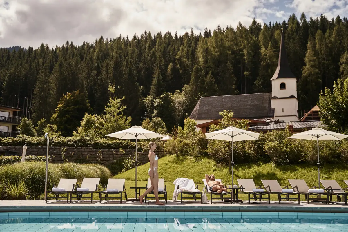 Liggen in de aja Werfenweng Een vrouw loopt langs een zwembad waar ligbedden staan.