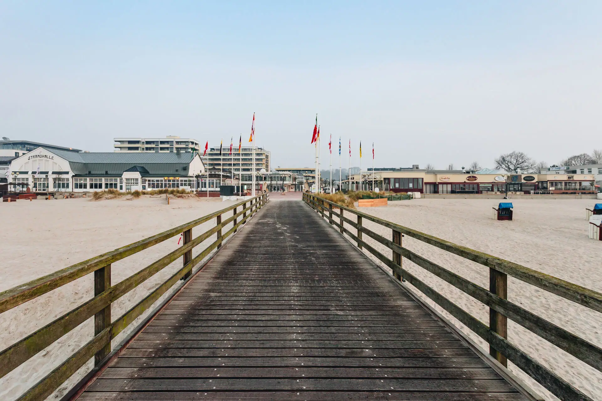 Holzbrücke über einem Strand mit klarem Himmel im Hintergrund.