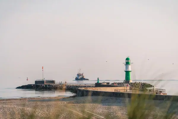 Leuchtturm am Strand bei klarem Himmel und Wasser im Hintergrund.
