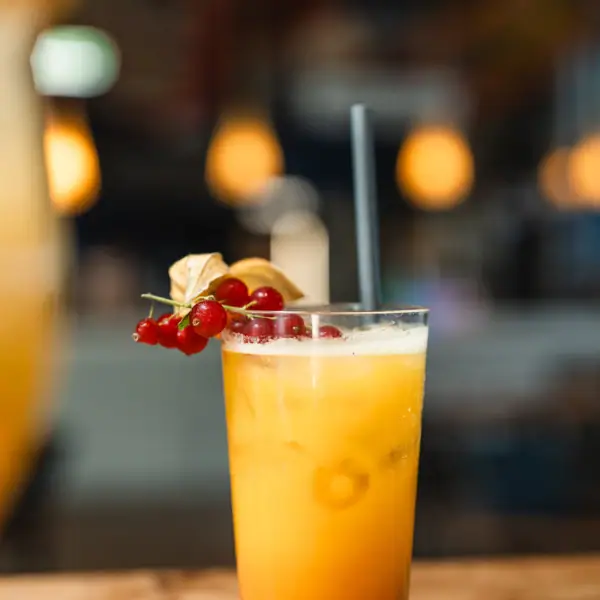 Drankjes bij aja Warnemünde Een glas met een sinaasappeldrankje, een rietje en bessen.