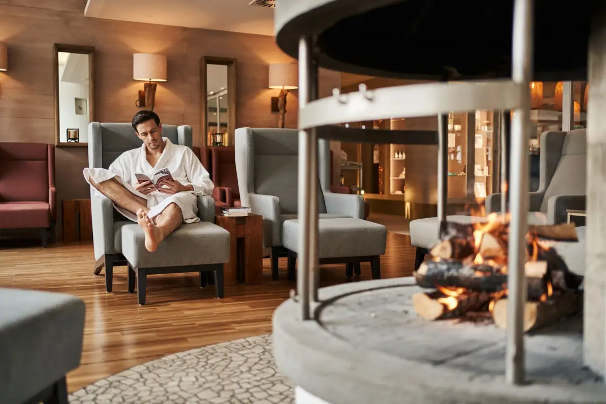 Open haard in de SPA Een man in een badjas zit in een stoel bij de open haard.