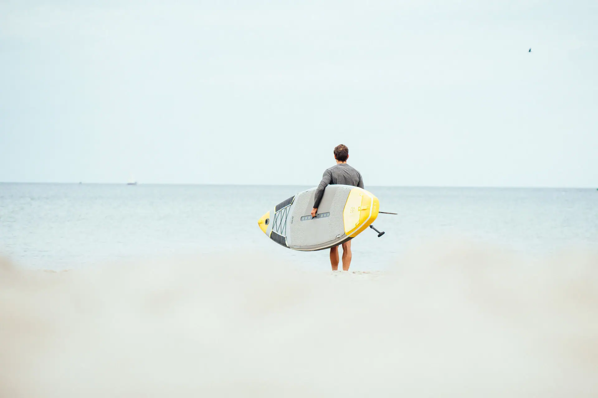Een man houdt een surfplank vast op het strand.