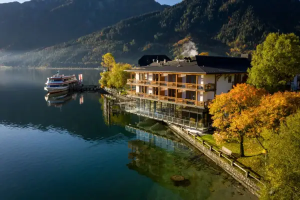 Gebäude am Wasser mit Bäumen und Bergen im Hintergrund.