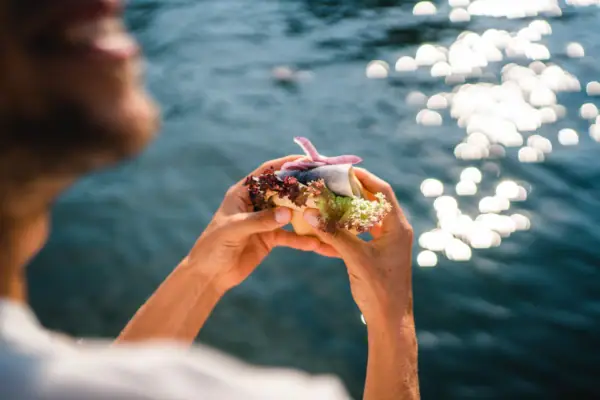 Fischbrötchen Eine Person hält ein Sandwich, im Hintergrund ist Wasser zu sehen.