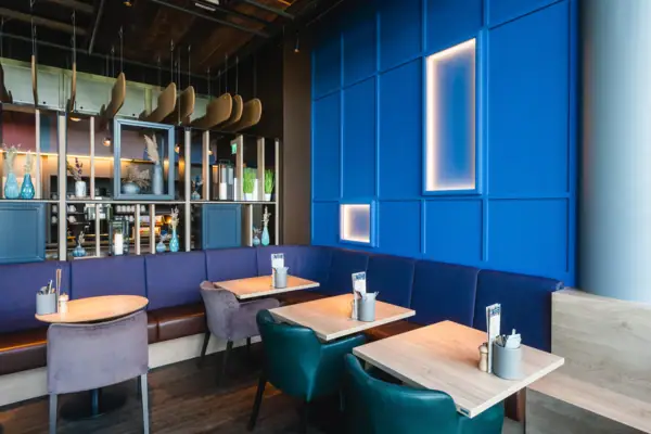 Blaue Sitzbank mit Tischen und Stühlen in einem Innenraum.