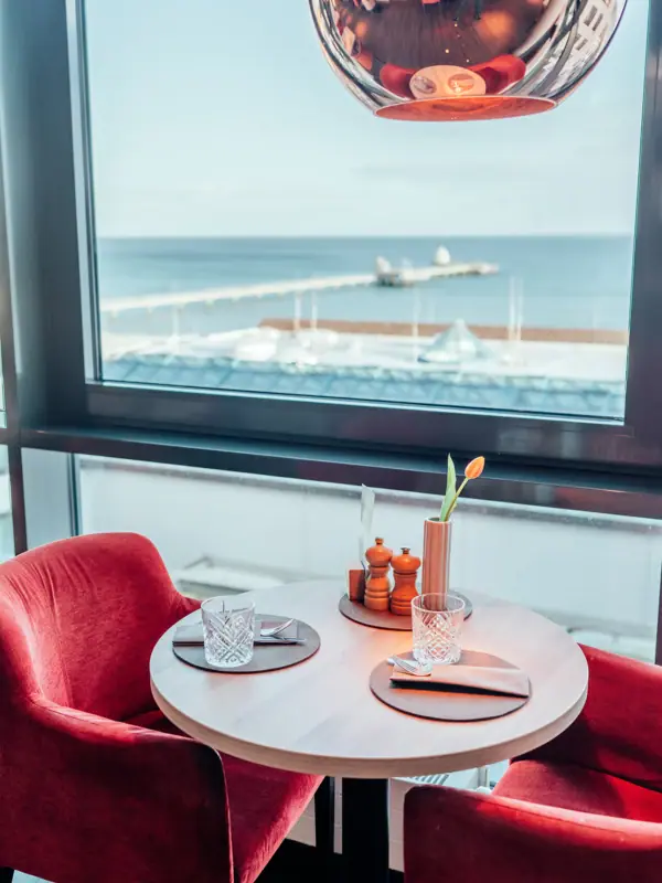 Uitzicht vanuit restaurant JEDERMANNS in Grömitz Een tafel met rode stoelen en een rode lamp.