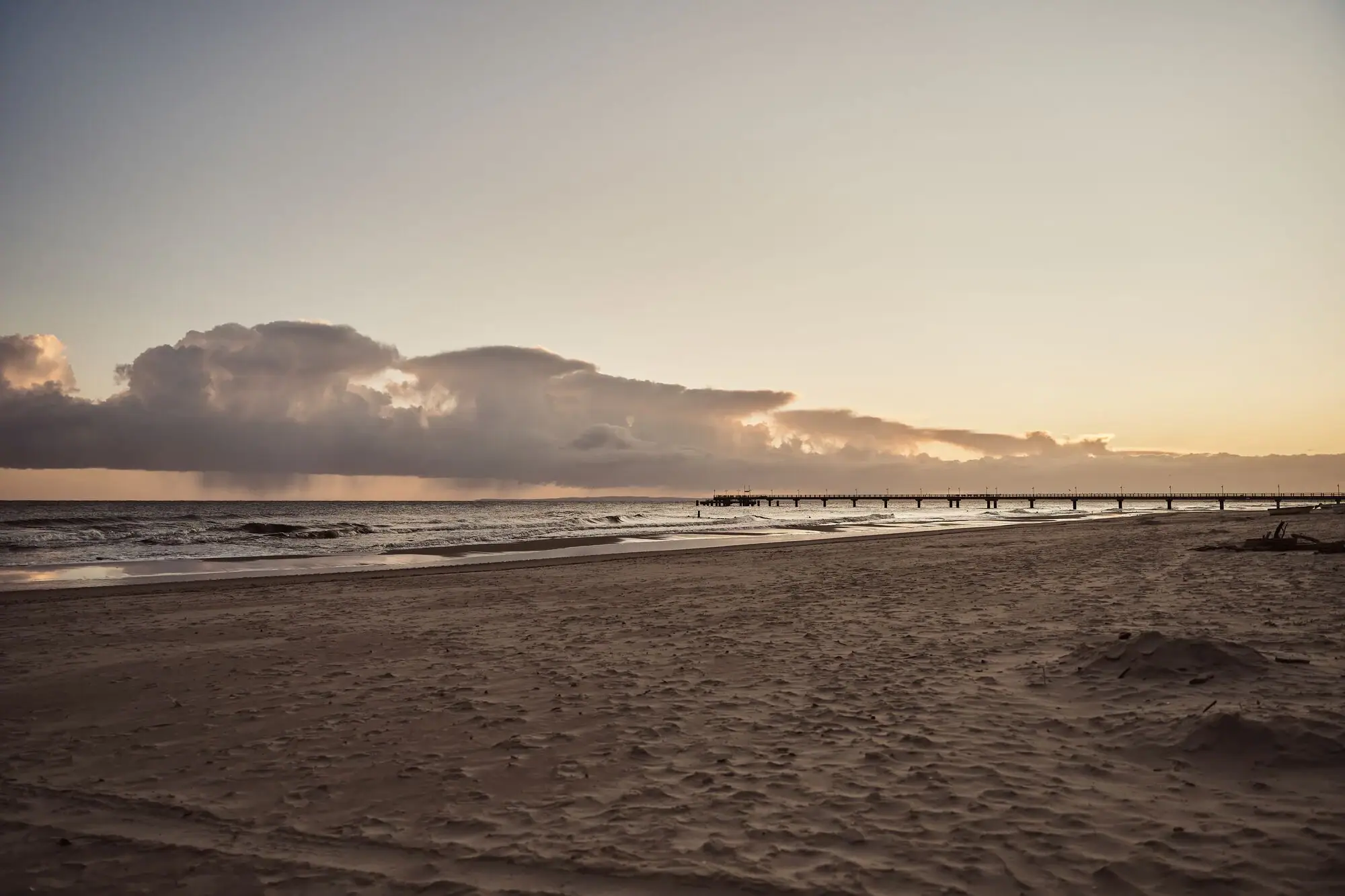 Een strand met een pier en water op de voorgrond.