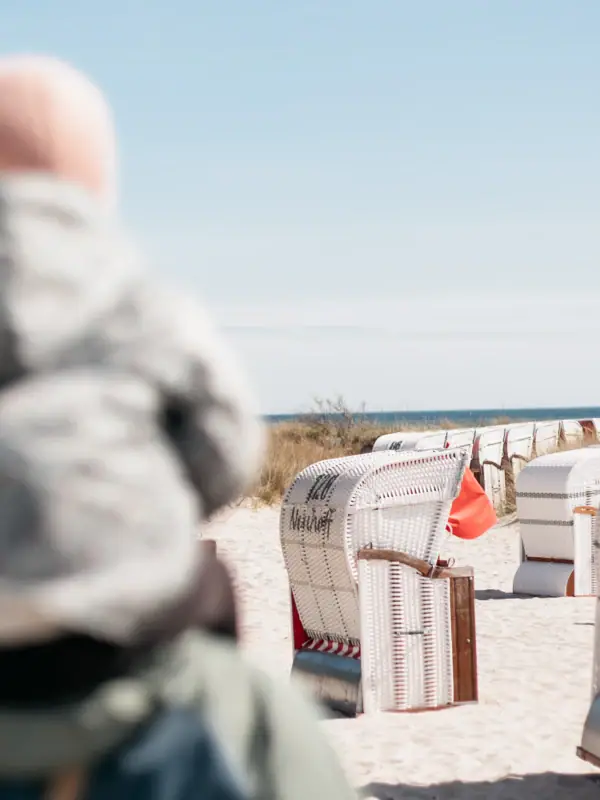 Een persoon met een baby op de rug op het strand.