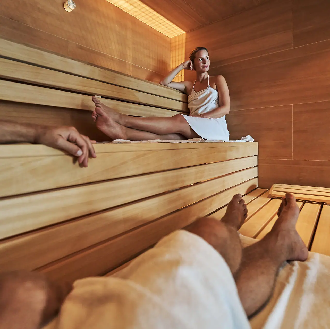 Een vrouw zit op een houten bank in een sauna.
