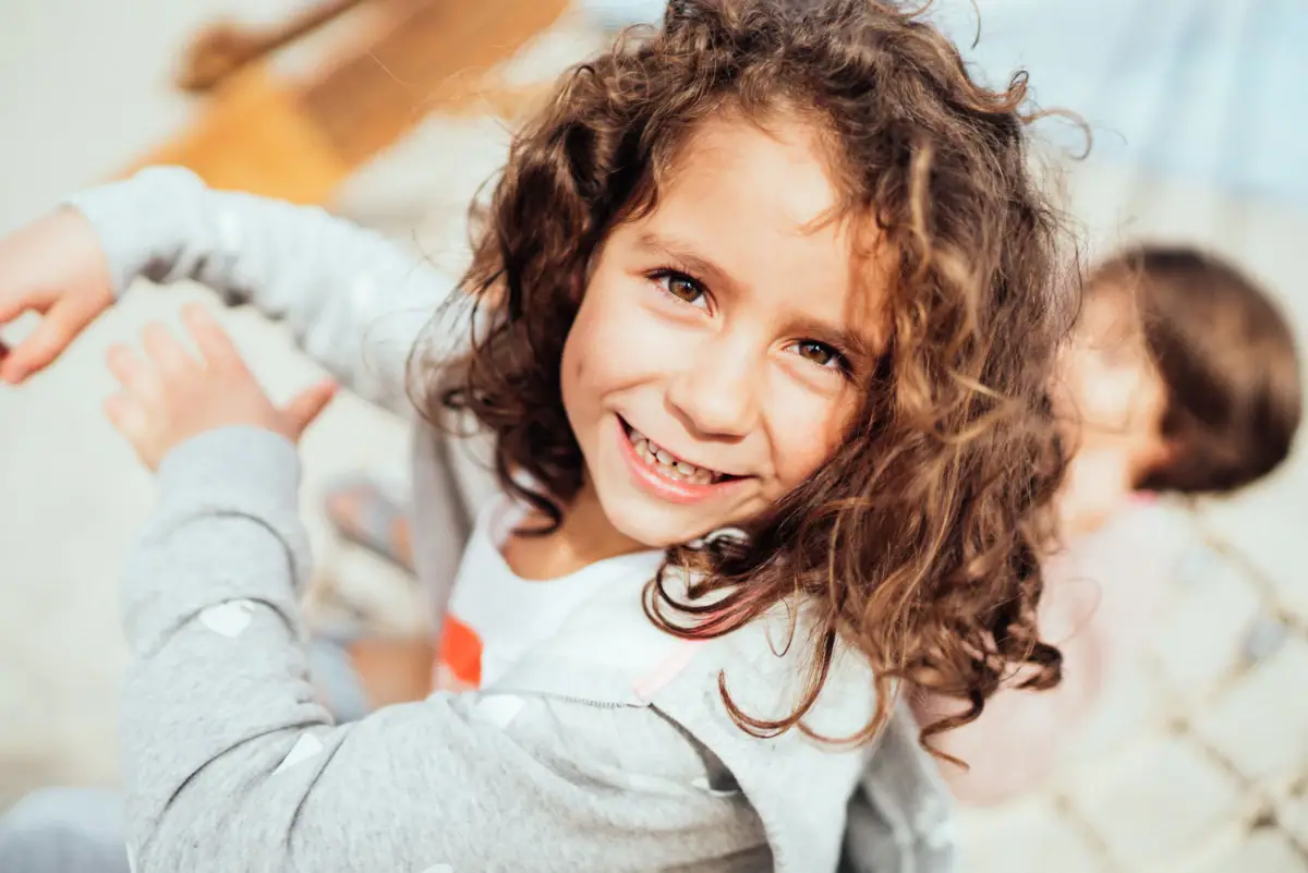 Een meisje met krullend haar glimlacht.