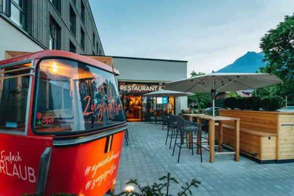 Terras aja Garmisch-Partenkirchen Het terras voor de aja Garmisch-Partenkirchen met een gondel en wat zitplaatsen en bergen op de achtergrond.