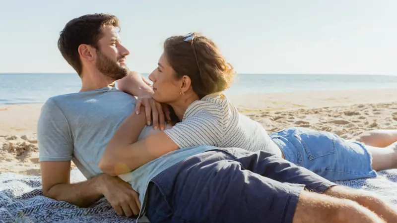 Een man en vrouw liggen op het strand in een romantische omhelzing.