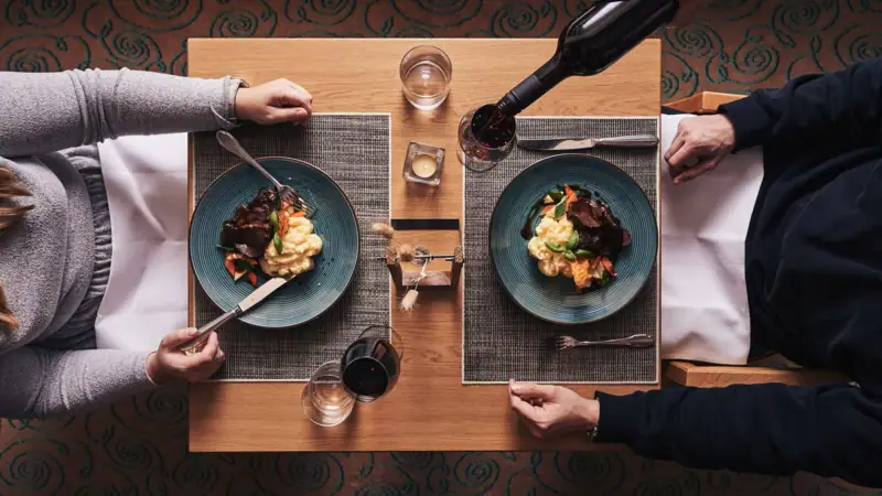 Diner Nordperd & Villa's Iemand houdt een fles wijn vast en eet.