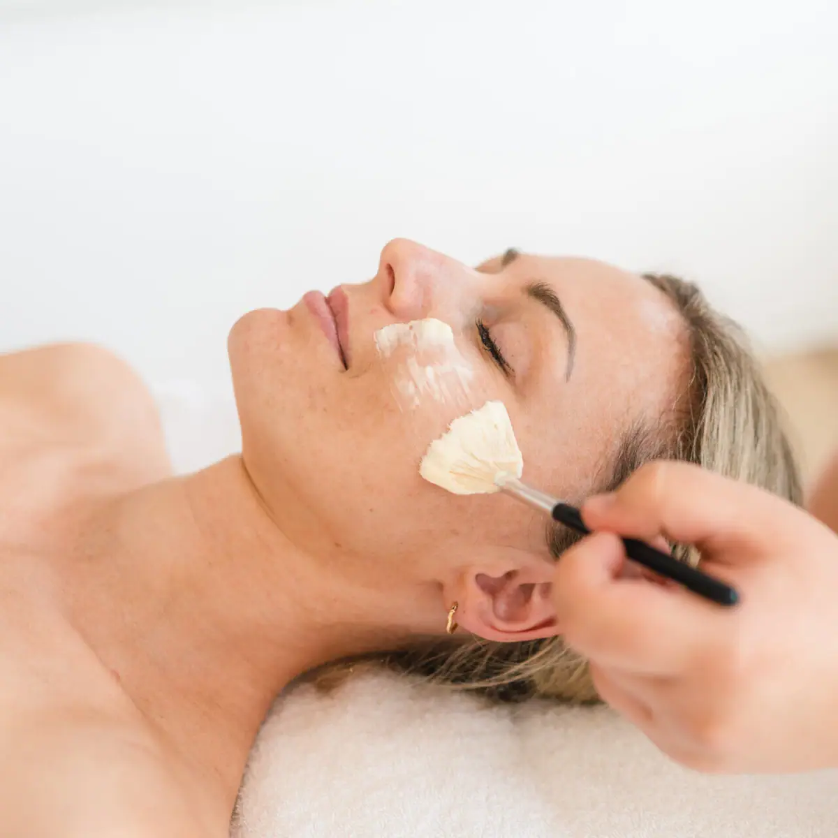 Toepassing op het gezicht Een vrouw ligt met een verfkwast op haar gezicht.