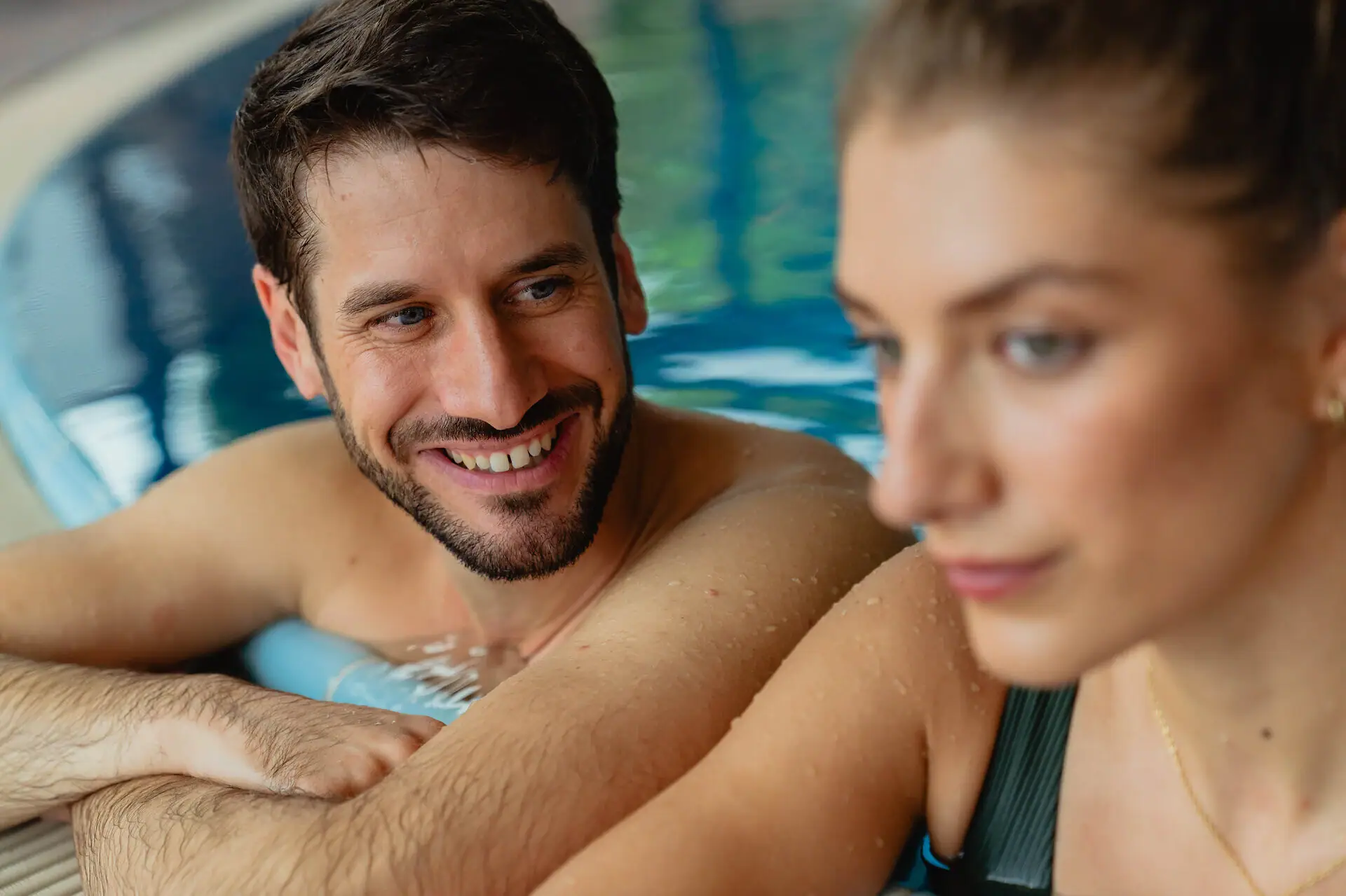 Een man en een vrouw in een zwembad, beiden glimlachend.