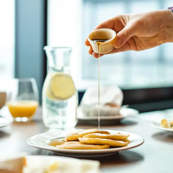 Eén persoon giet stroop op een bord pannenkoeken.
