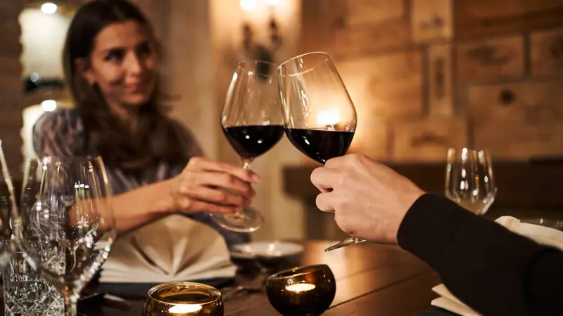 Een man en een vrouw proosten met hun wijnglazen aan een tafel.