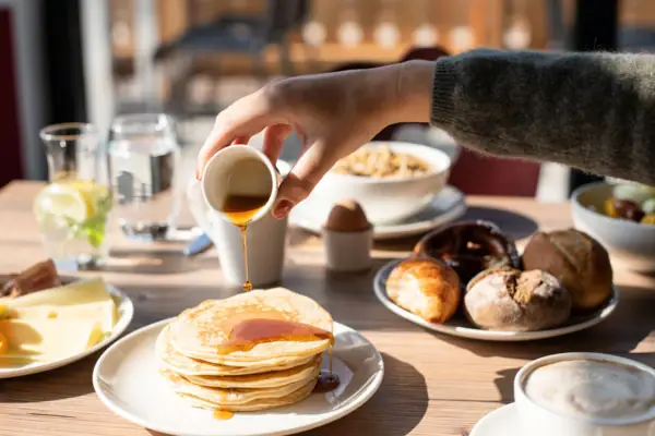 Eén persoon giet stroop op een stapel pannenkoeken.