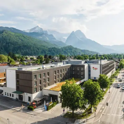 aja Garmisch Een gebouw met bomen en bergen op de achtergrond.
