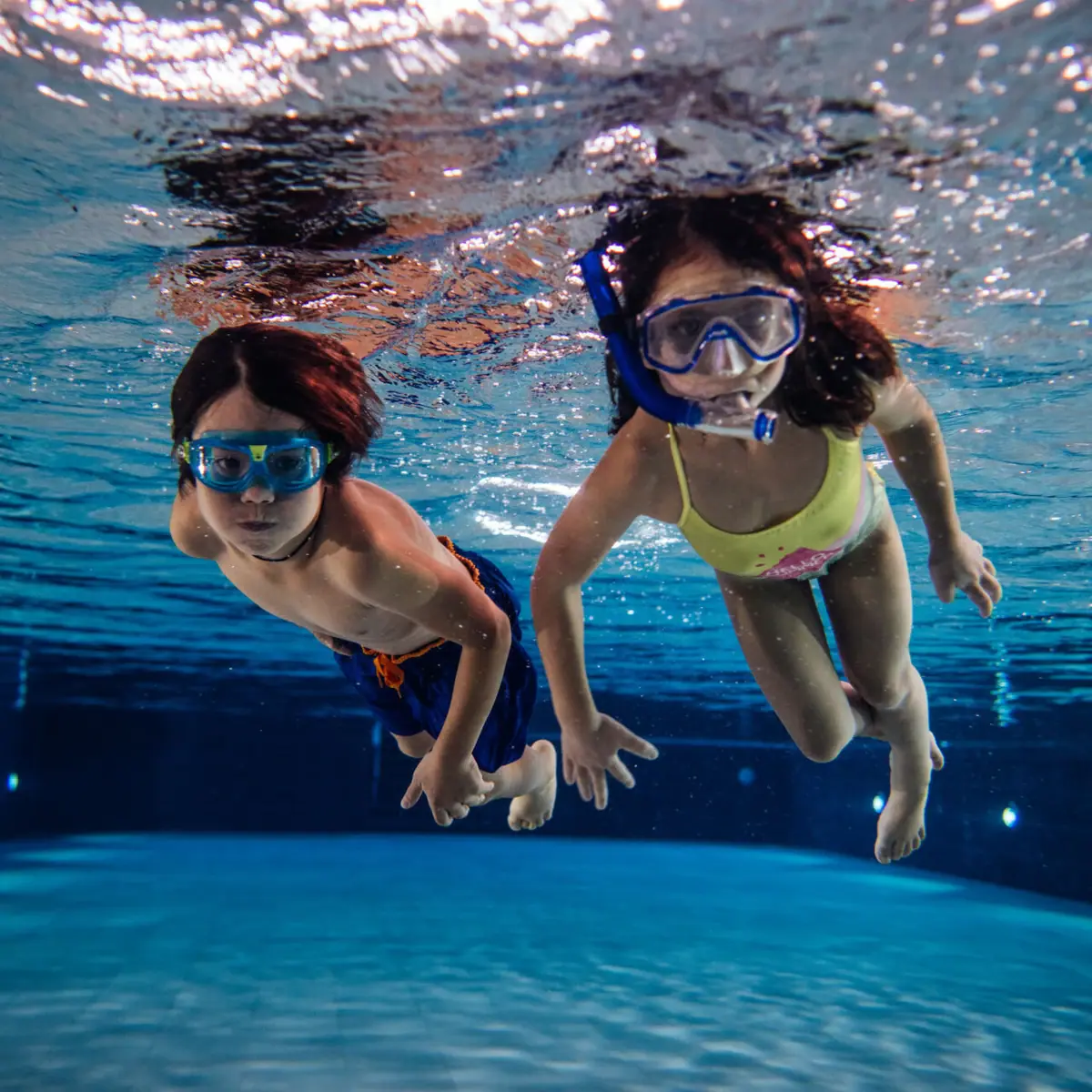 Zwemmen Twee kinderen zwemmen onder water in een zwembad.