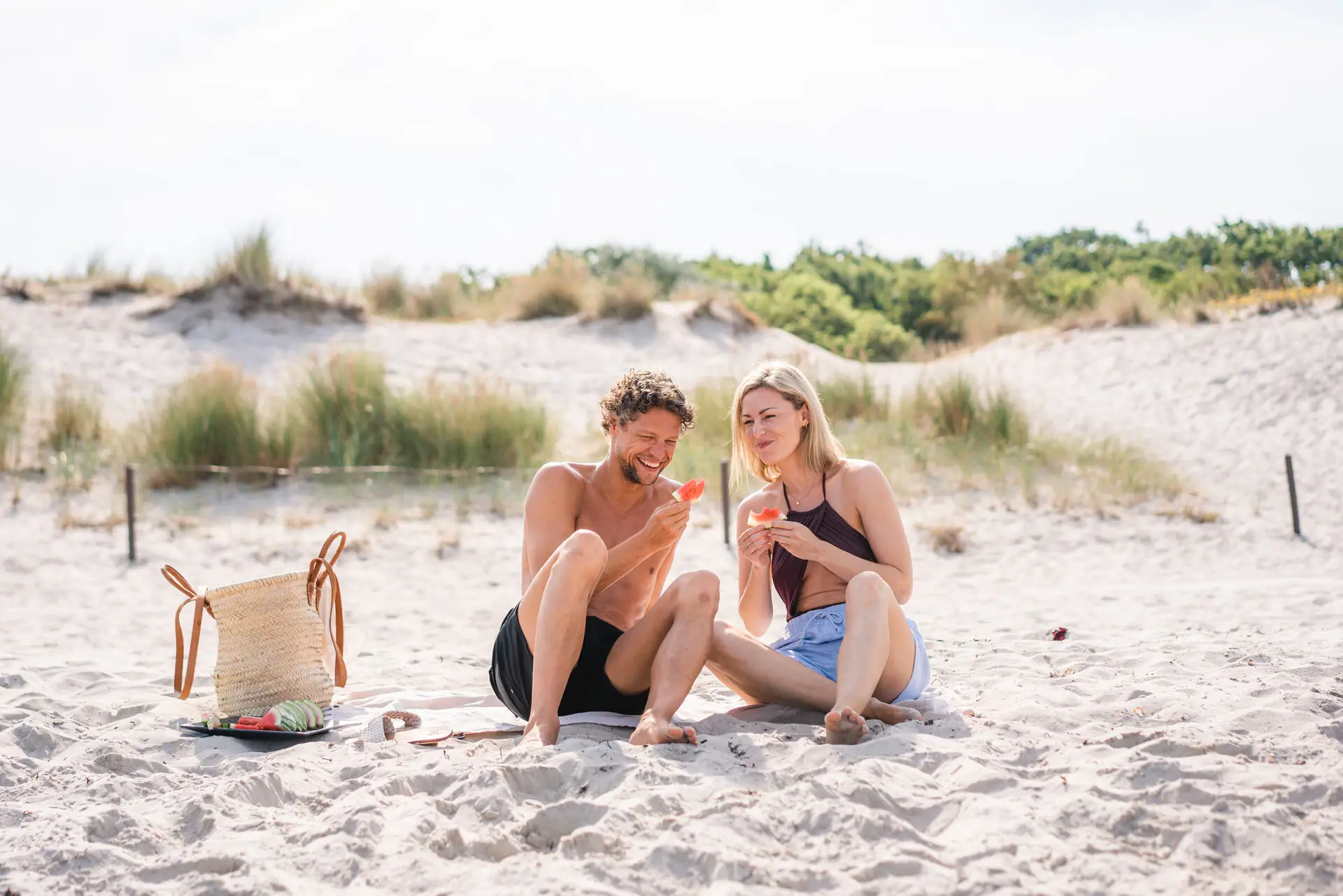 Een man en een vrouw zitten op het strand watermeloen te eten.