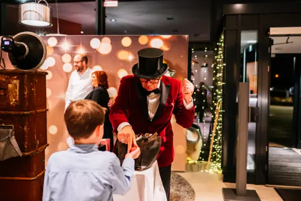 Een man in een rood pak overhandigt een geknoopte ballon aan een jongen.