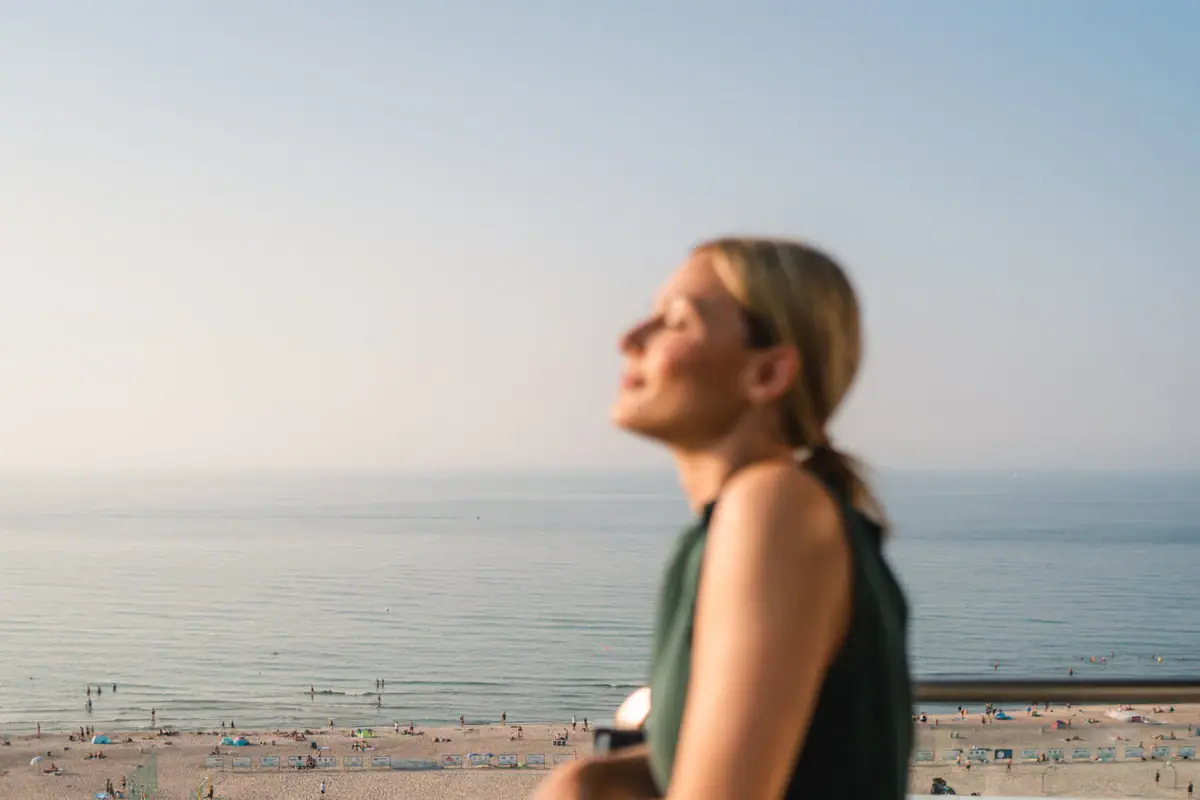 Een vrouw staat op een reling en kijkt uit over een strand.