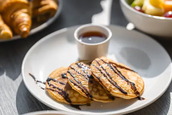 Een bord met pannenkoeken en stroop en een beker met stroop.