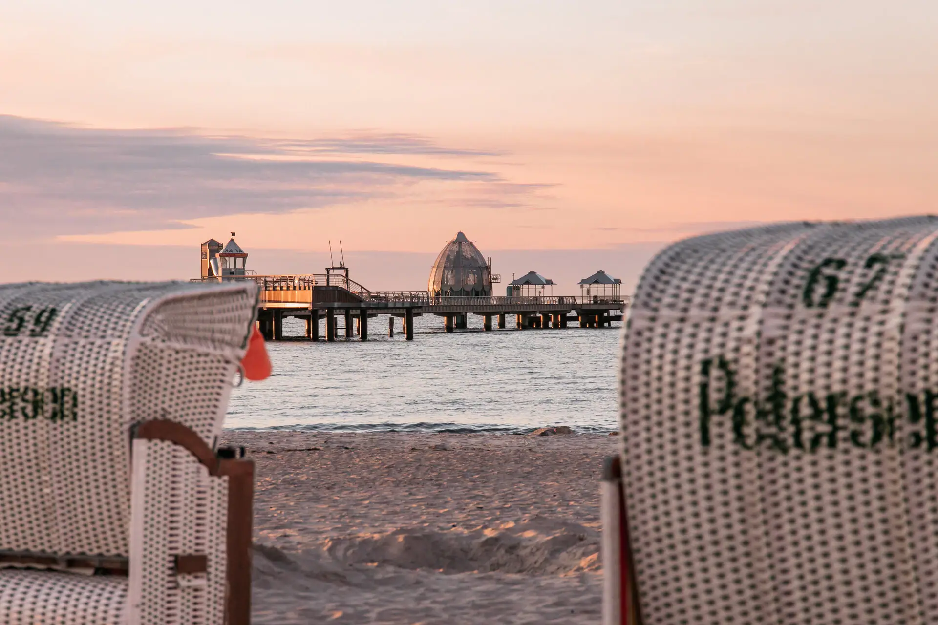 Een strandstoel op het strand met een pier op de achtergrond.