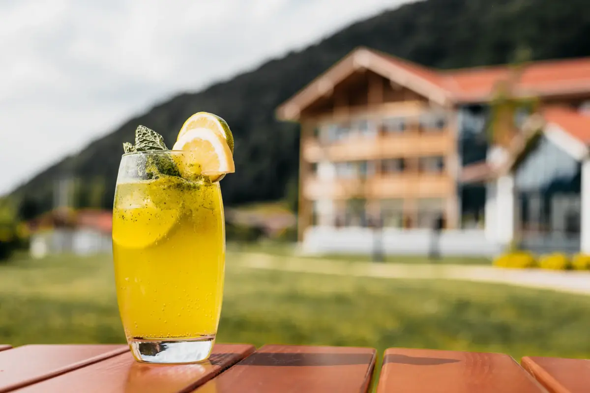 Een glas gele vloeistof, gegarneerd met een schijfje citroen en munt, op een tafel.