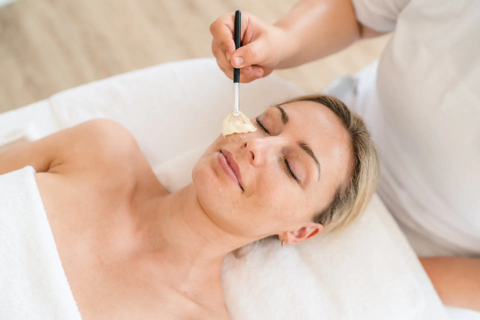 Cosmetica bij aja Grömitz Een vrouw ligt met een verfkwast op haar gezicht.