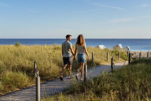 Wandelen op Usedom Een man en een vrouw houden elkaars hand vast en lopen over een pad langs het water.