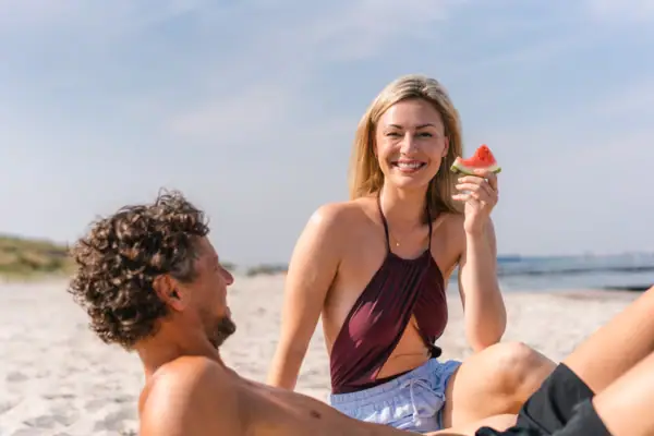 Warnemünde Strand Eine Frau hält ein Stück Wassermelone, während sie am Strand sitzt.