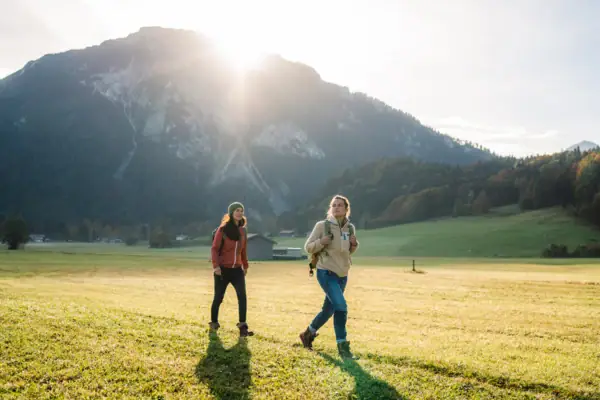 Twee vrouwen wandelen in een veld met bergen op de achtergrond.
