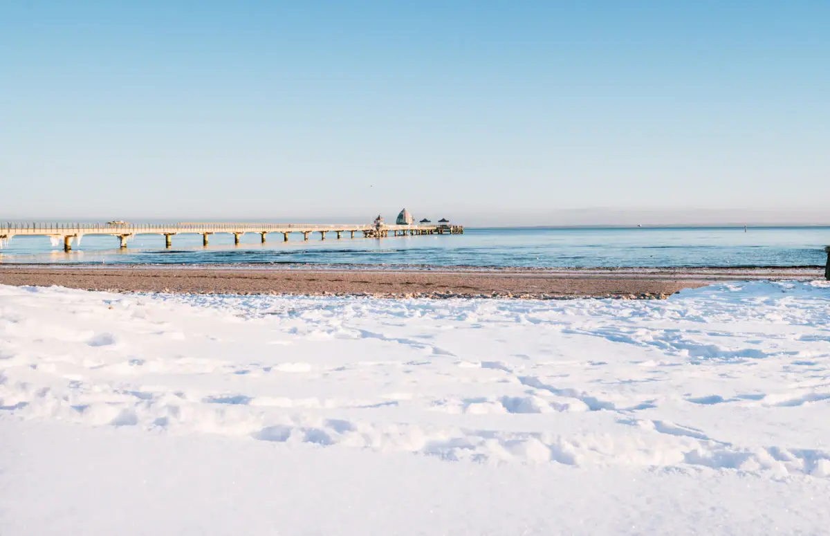 Strand in de winter Een met sneeuw bedekt strand met een steiger en water in de winter.
