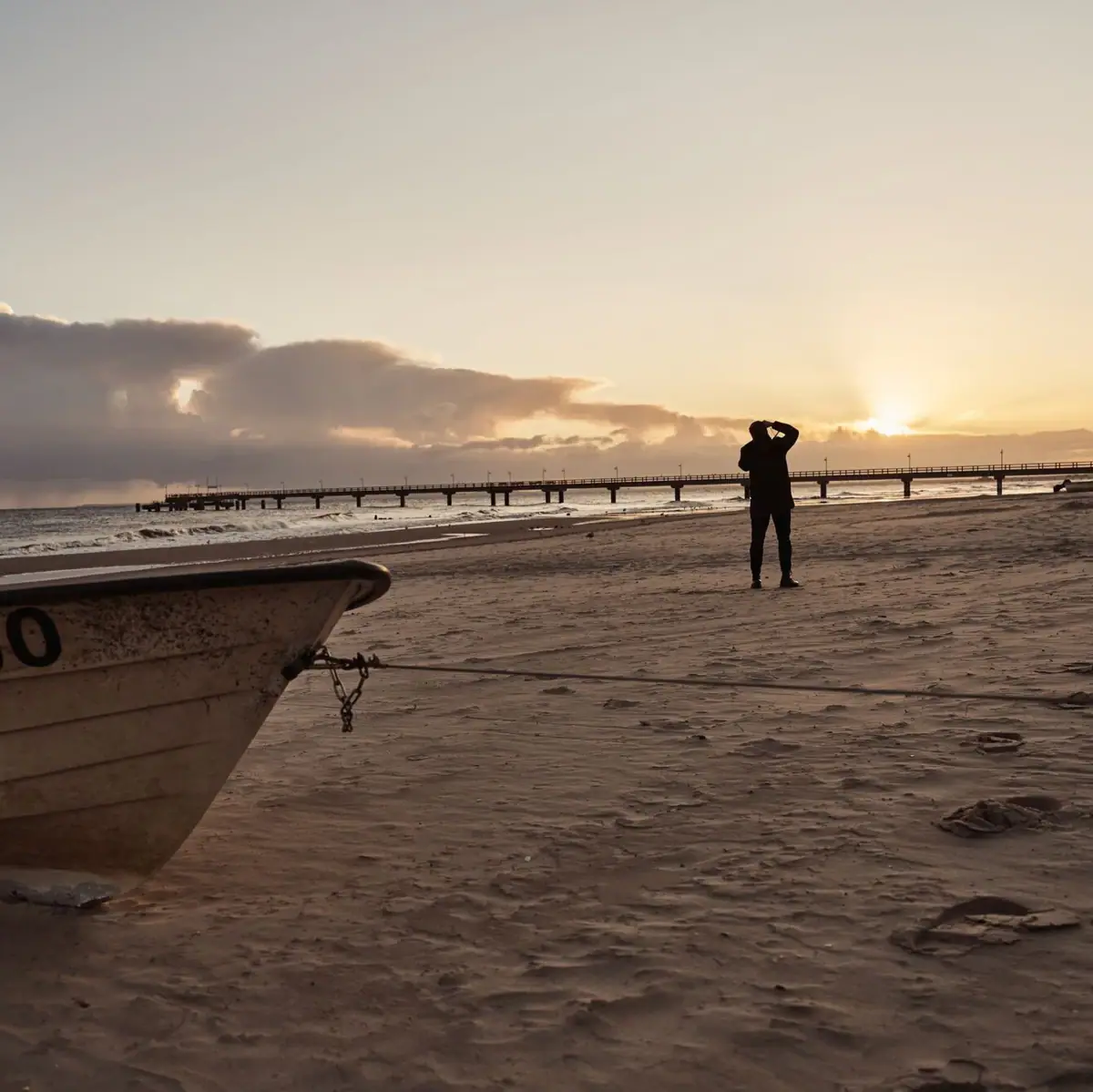 Persoon op het strand met boot op de oever.