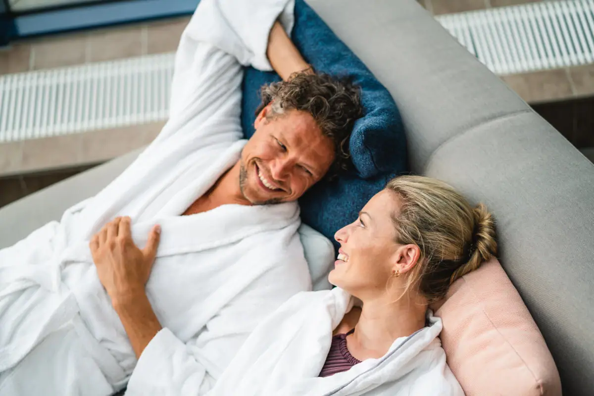 Een man en een vrouw liggen glimlachend op een bank.