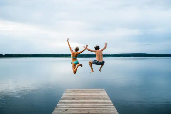 Ein Mann und eine Frau springen von einem Steg in einen See.