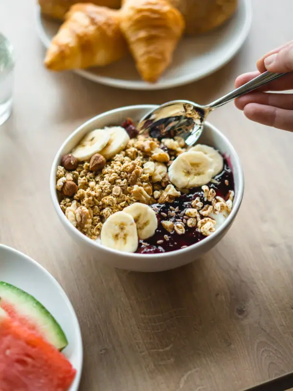 Een kom met granola, fruit en een lepel.