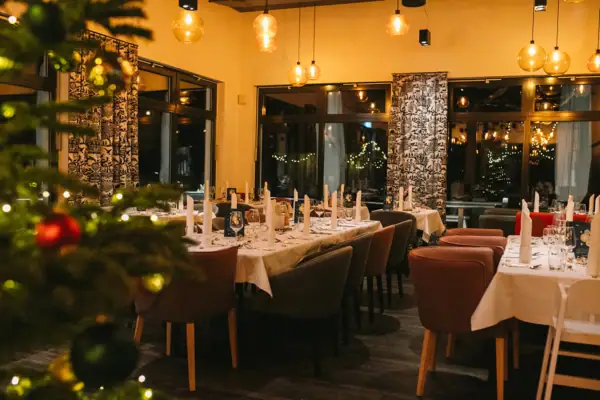 Een kamer met tafels en stoelen, feestelijk versierd en een kerstboom op de voorgrond in de onscherpte.