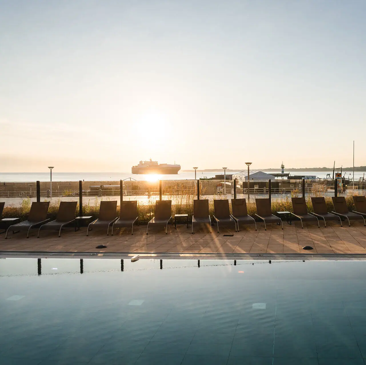 Buitenzwembad aja Travemünde Een zwembad met stoelen en een boot op de achtergrond.