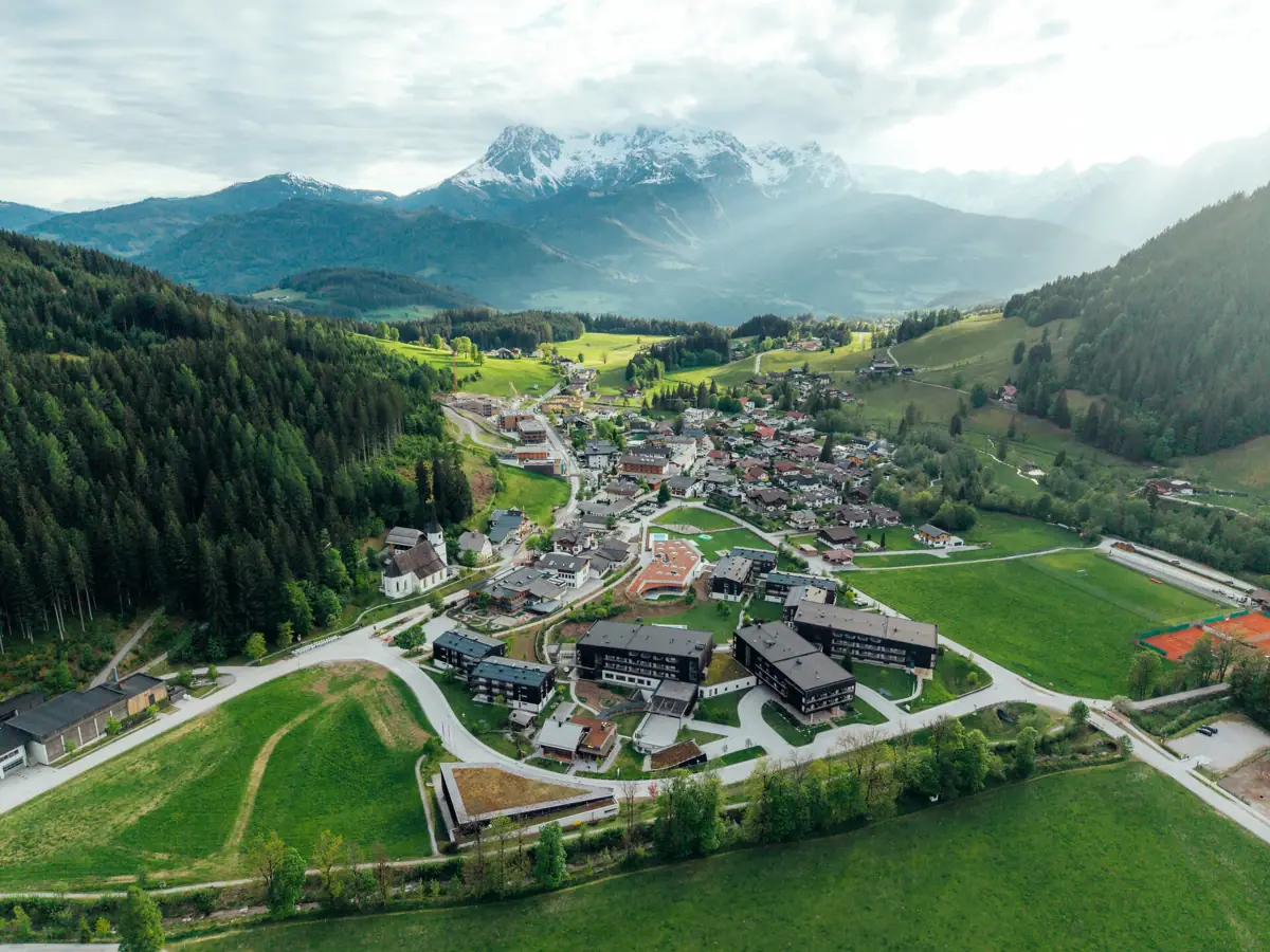 aja Werfenweng Mountain Resort Een bergdorpje met huizen die verscholen liggen tussen de bomen en omringd zijn door bergen.