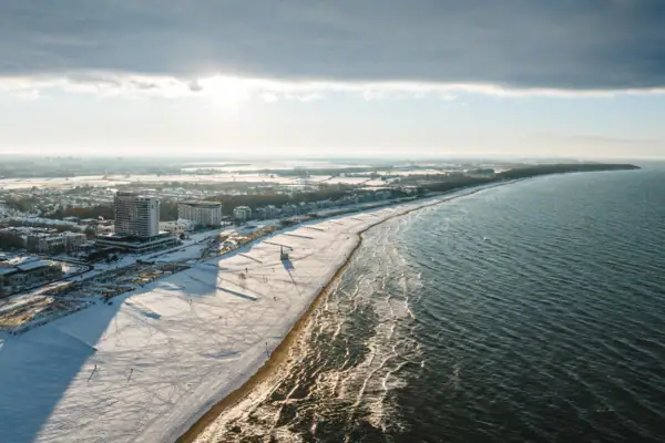 Ein schneebedeckter Strand mit Gebäuden und Wasser im Hintergrund.