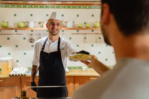 Een man met een koksmuts geeft een andere man een bord eten.