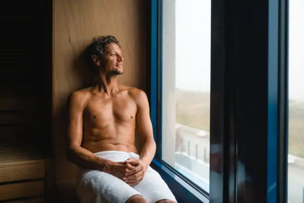 Sauna bij aja Warnemünde Een man zit op een bankje in de sauna en kijkt uit het raam.