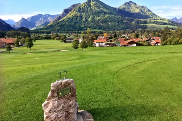 Golfbaan Ruhpolding Een steen in een weiland met een groep huizen op de achtergrond.