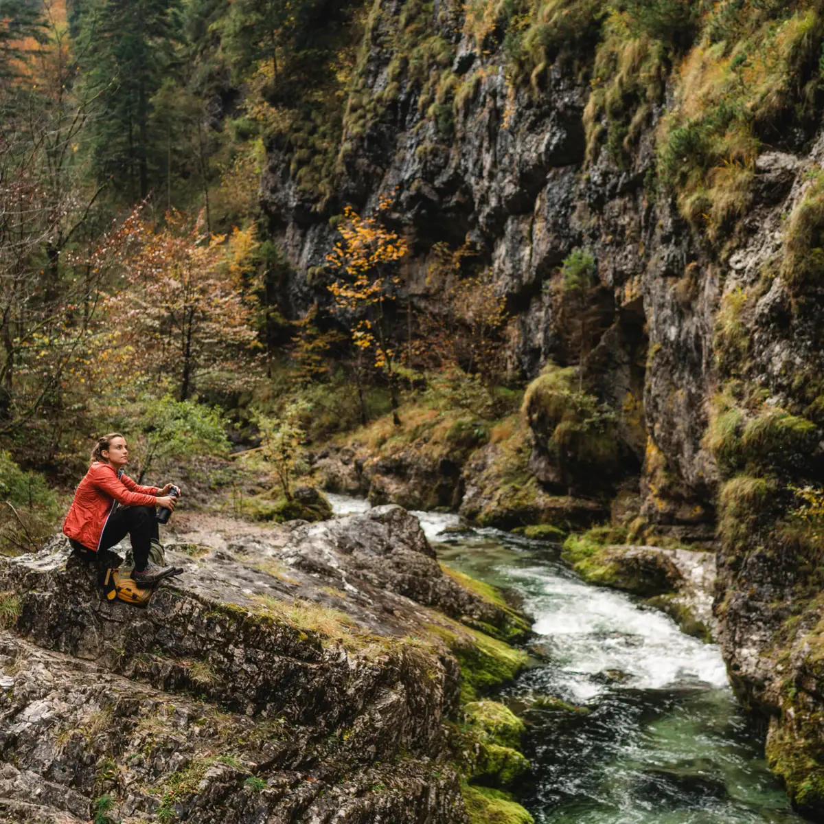 Een vrouw zit op een rots aan de rivier in de Weißbachschlucht.